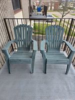 Two green plastic Muskoka chairs placed side by side on a balcony with railing and outdoor view.