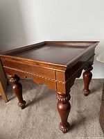 Side view of one solid wood end table showing carved decorative trim, scalloped apron, and turned claw-foot legs.