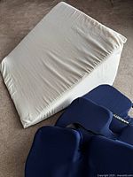 Large white foam wedge pillow and two blue KABOOTY foam seat cushions on carpeted floor.