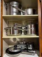 View of multiple stacked stainless steel pots and pans of various sizes on shelves.