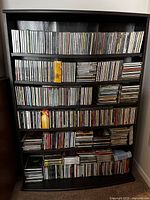 Front view of black shelving unit densely filled with CD jewel cases arranged in rows and stacks on five shelves