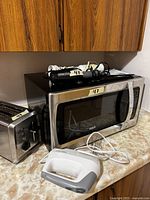Photo showing RCA microwave with digital controls, Hamilton Beach toaster and Black & Decker hand mixer on countertop.