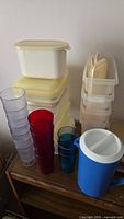 Photo showing stacked Tupperware containers and various colored plastic drinking cups on a wooden surface.