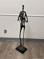 Front view of an abstract iron and bronze sculpture of a person playing a saxophone, showing extended limbs and saxophone detail.