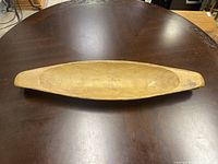 Top view of the hand-carved wooden canoe bowl placed on a round wooden table showing its full length and shape.