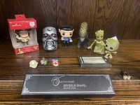Collection of collectibles including boxed Hallmark Walking Dead figure, Terminator skull, Star Trek Spock, Alien, Groot figures, Severus Snape wand pen, business card holder, and pins displayed on wooden surface.