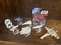 Overview of Star Wars die-cast starship models including Millennium Falcon, Slave I, X-Wing, TIE Fighter, and others on clear stands with one TIE Fighter in original packaging.