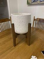 Front angle showing the full planter pot with black speckled pattern and wooden stand on a wooden table.