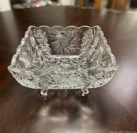 Front angled view showing intricate starburst and geometric cut patterns on clear crystal dish, scalloped edge, and feet visible.