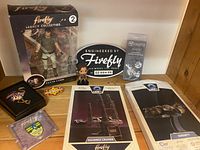 Overview of Jayne Cobb action figure (boxed), character figure, license plate plaque, model kits brochures, and pins displayed on wooden shelf.