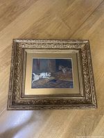 Frontal photo of framed painting showing two dogs inside barn, ornate wooden frame visible.