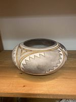 Side view of round ceramic pot with gray, gold, and white geometric Aztec pattern.