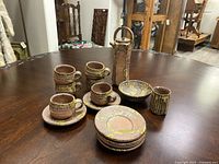 Complete view of 6 cups, 6 saucers, and other pieces on wooden table, showing glaze and craftsmanship.