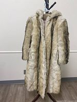 Front view of large fur coat with beige and brown fur, hanging on stand.