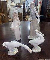 The full set of four porcelain figurines on a table, two human figures and two geese.