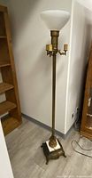 Full view of vintage brass and glass floor lamp showing tall, slender brass stem, glass shade, four bulb holders, and ornate base.