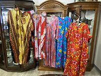 Five multicolour floral and abstract patterned caftan muumuu house dresses hanging on a rack alongside a small matching purse, displayed for condition and details.