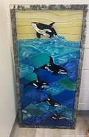 Full view of the rectangular stained glass panel with orca whale design, framed in textured silver-gray metal.