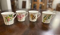 Front and top view of four Royal Grafton fine bone china teacups each with different floral designs, arranged on a wooden surface showing classic shape and color details.
