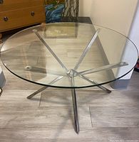 Top front angle view showing clear round glass top and starburst silver metal base with five legs.