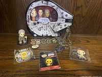 Millennium Falcon tin with Star Wars Pez dispensers and loose Star Wars pins, patches, keychains, and figurines displayed on a wooden surface.