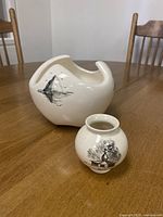 Photo showing both off-white ceramic pottery bowl and vase with black hand-painted designs on wooden table