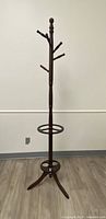 Full front view of dark brown wooden coat rack showing base, umbrella holder, and multiple hooks.