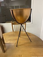 Front-facing photo of copper bowl on a black metal tripod stand placed on a wooden table.