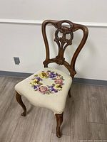 Full view of the antique chair showing wooden carved backrest and floral needlepoint upholstered seat.