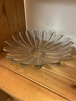 Clear glass flower-shaped bowl photographed from an angled front view on a wooden surface, showing its petal-like design and glossy finish.
