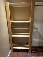 Front view of the three-shelf wooden unit showing its full height against a wall, with natural wood color and visible construction details.