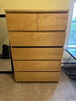 Front view of the 5-drawer light wood dresser with all drawers visible and minor damage to one drawer.