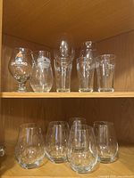 Shelf of assorted clear glassware including Ontario branded snifter, cocktail shakers, pint glass, and other drinking glasses.