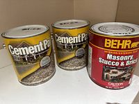 Photo showing two yellow CementPak masonry sealer cans labeled 'Brick' and a red BEHR Masonry, Stucco & Brick paint can.