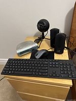 Full view of assorted tech gadgets on a wooden drawer including keyboard, mouse, clock radio, microphone, and speakers