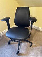 Front view of black faux leather office chair showing padded seat, adjustable armrests, and swivel base with casters.