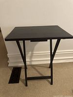 Front view of black folding side table showing flat rectangular top surface and X-shaped folding legs.