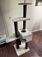 Full side view of the three level cat tree with beige carpet covering and four dark brown scratching posts, standing on wooden floor.