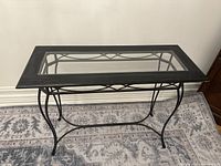Side view of the black metal and glass entryway table showing curved metal legs and glass top.
