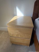 Front view of light wood nightstand showing two drawers and visible scratches.