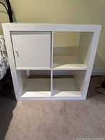 Front view of the white shelving unit showing four compartments with one door on top left.