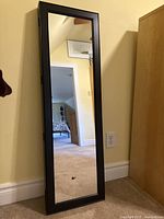 Closed view of tall black framed jewelry case with full-length mirror reflecting room.