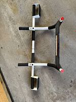 White and black metal pull-up bar with foam grips placed on floor, showing condition and materials.