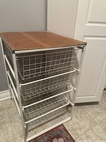 Front angled view showing three white metal wire basket drawers and composite wood top, floor standing unit.