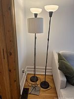 Three standing lamps including one with fabric shade and two torchiere lamps with glass bowl shades, corner placement by couch and wall with wood trim.