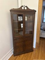 Full view of the traditional wooden display cabinet with glass upper doors and wooden lower doors, placed against a wall showcasing overall design and dimensions.