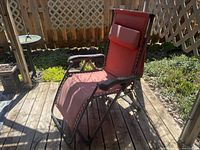 Side view of one red anti-gravity chair on patio wood deck showing fabric, black metal frame, and armrests.