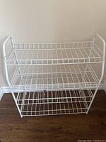 Front view of white wire shoe rack showing three tiers of wire shelves and open wire frame sides.