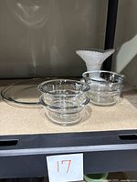 Four clear Anchor Hocking glass bowls stacked and one milk glass hobnail candy dish at the back on a shelf.