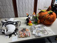 Overview photo showing four Annalee felt dolls, Halloween pins in bags, a large orange plush pumpkin, and a white ghost decoration with 'Boo!' pillow on table.